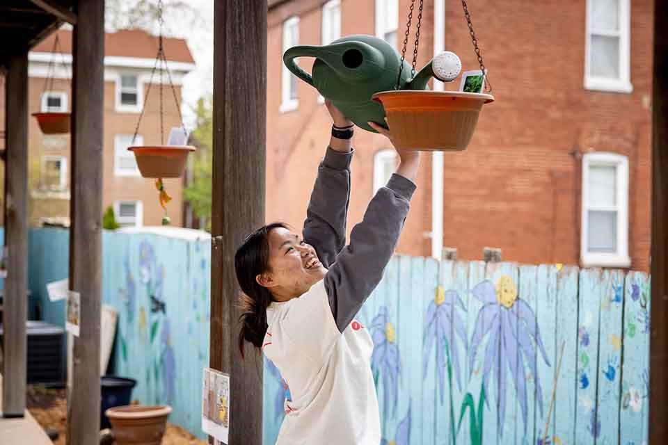 博彩网址大全 student volunteer watering a plant on a porch