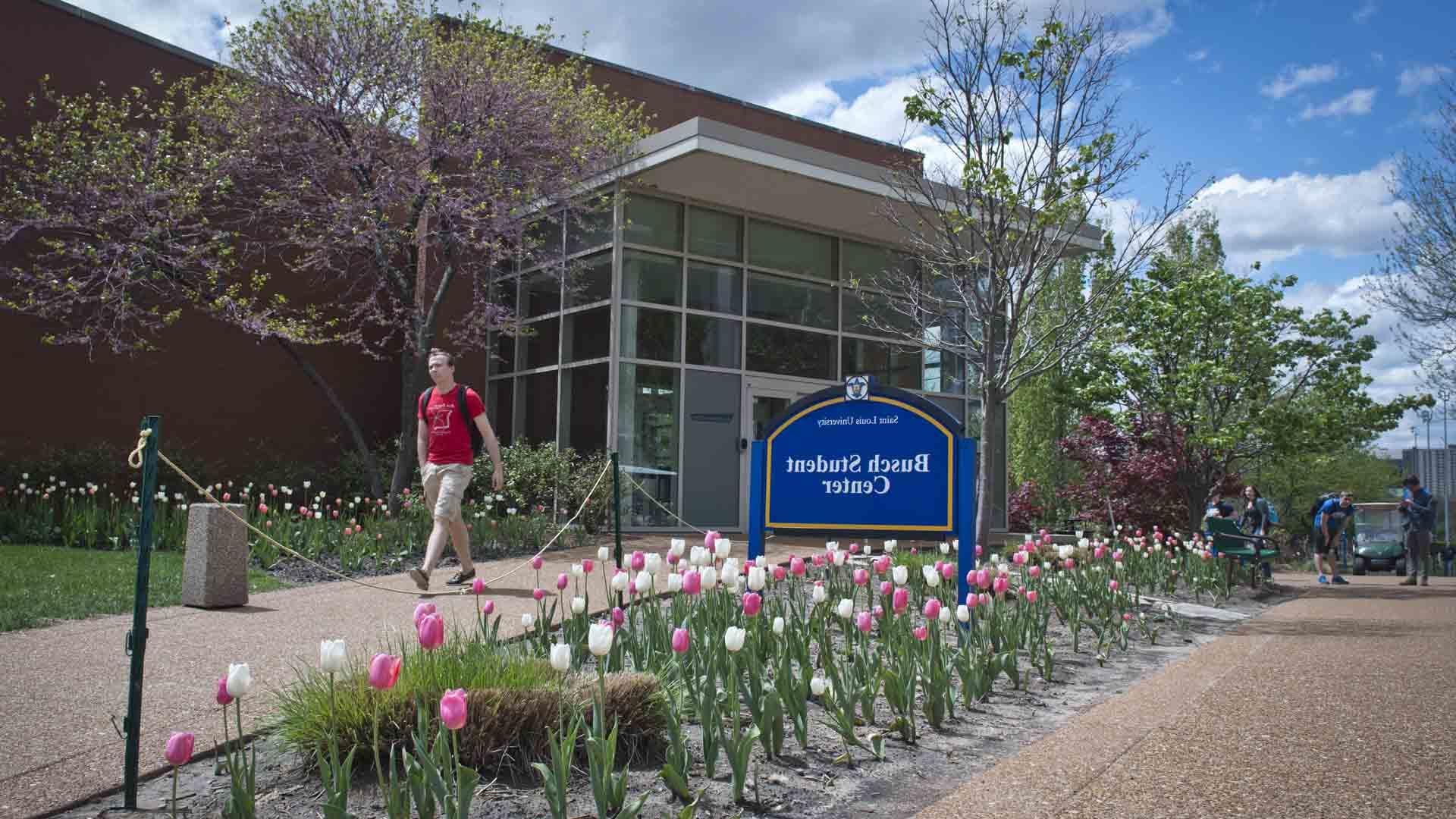 Exterior of the Busch Student Center with a student walking by and flowers blooming.