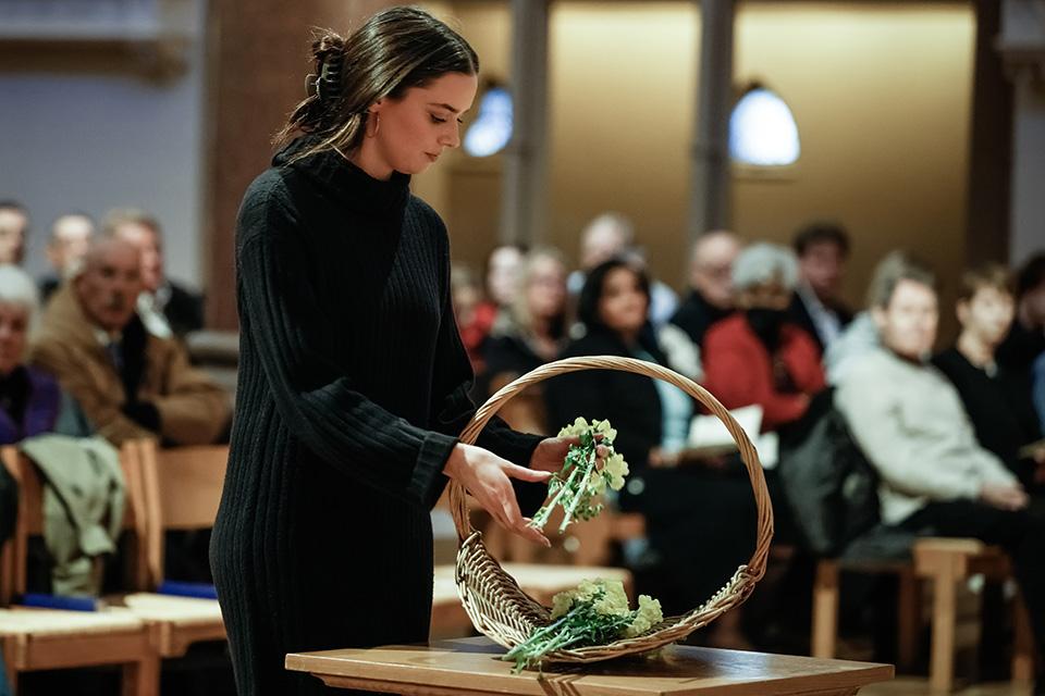 A young woman places flowers in a basket during a prayer service.